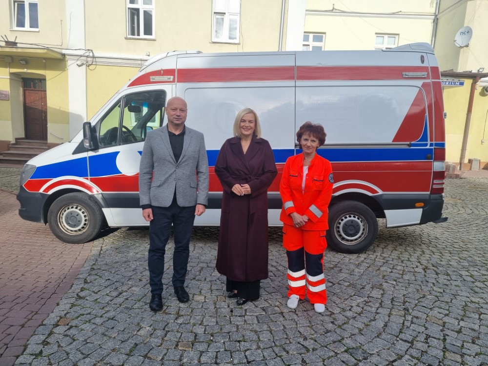 Trzy osoby (dwie kobiety, jeden mężczyzna) w tle bus dostawczy w malowaniu ambulansu