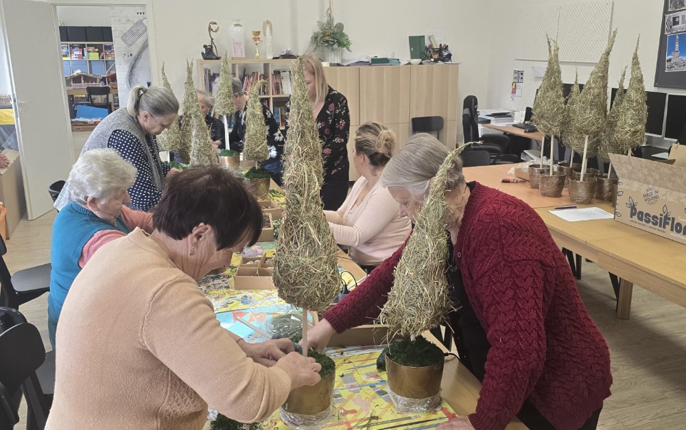 Zdjęcie przedstawia seniorów wykonujących choinki z siana