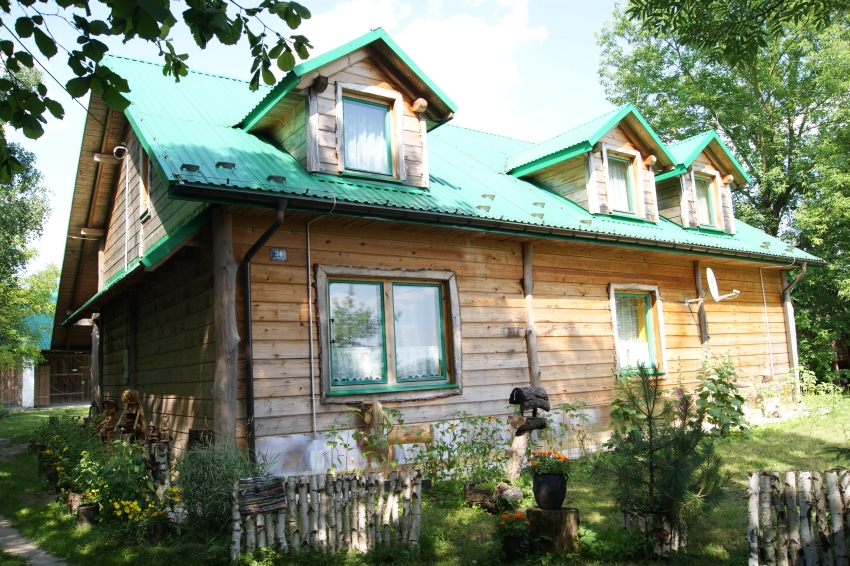 Drewniany dom z zielonym dachem, wokół niego drzewa